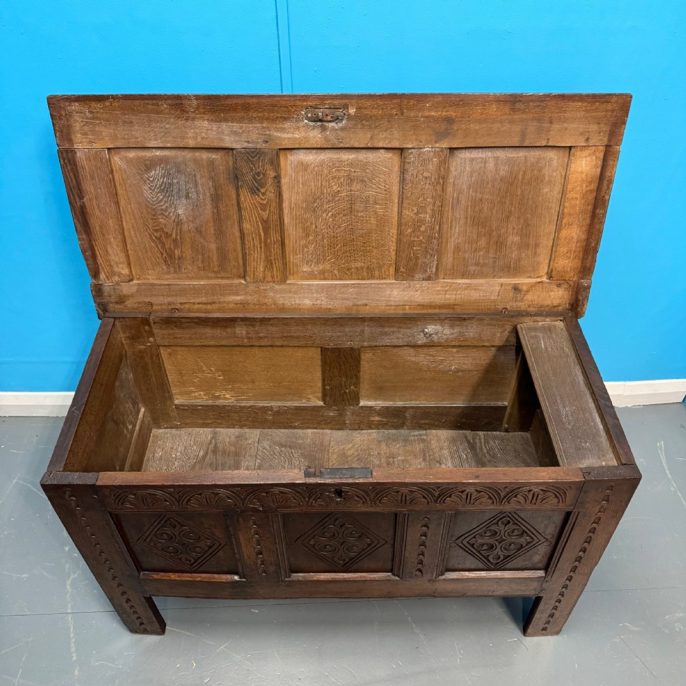 An 18th-century dark oak coffer featuring three carved diamond lozenge panels, an arcaded top rail, and a panelled hinged lid. View V
