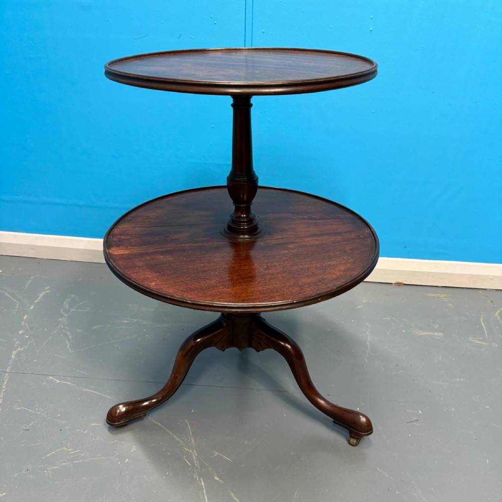 An 18th-century Georgian mahogany two-tier dumb waiter featuring circular tray surfaces, a central turned column, and a tripod base with castors.