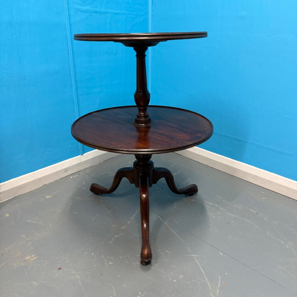 An 18th-century Georgian mahogany two-tier dumb waiter featuring circular tray surfaces, a central turned column, and a tripod base with castors. View II