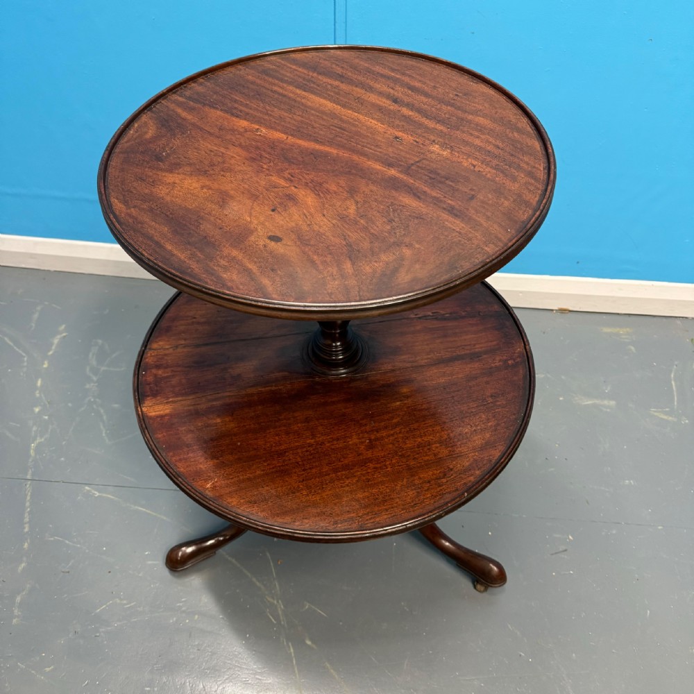 An 18th-century Georgian mahogany two-tier dumb waiter featuring circular tray surfaces, a central turned column, and a tripod base with castors. View V