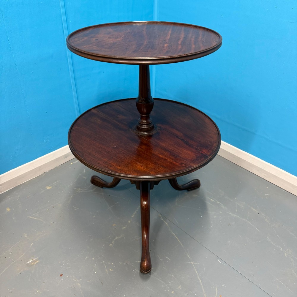 An 18th-century Georgian mahogany two-tier dumb waiter featuring circular tray surfaces, a central turned column, and a tripod base with castors. View VI