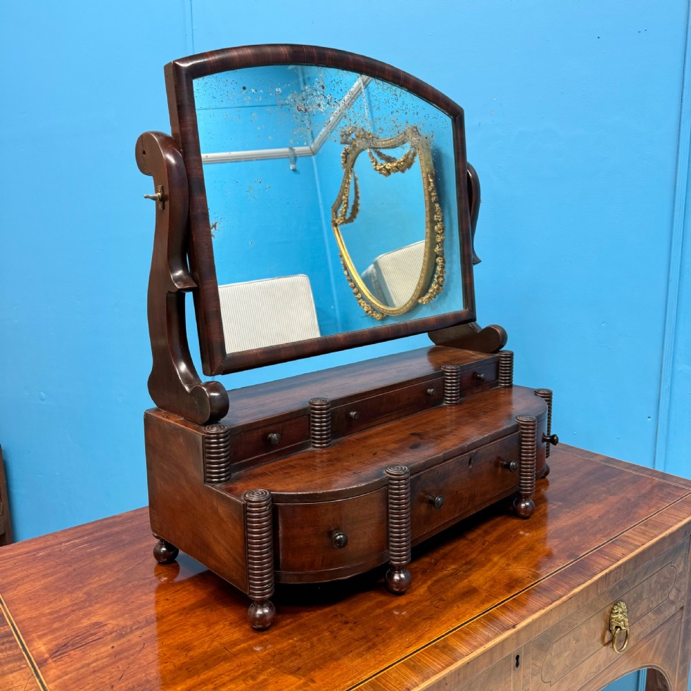 A Regency mahogany bow-fronted toilet mirror featuring an adjustable arched mirror glass supported by reeded pillars above integrated base drawers.