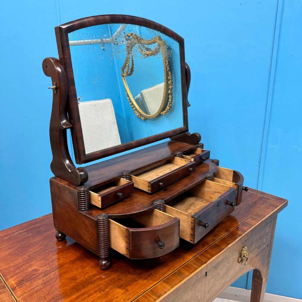 A Regency mahogany bow-fronted toilet mirror featuring an adjustable arched mirror glass supported by reeded pillars above integrated base drawers. View II