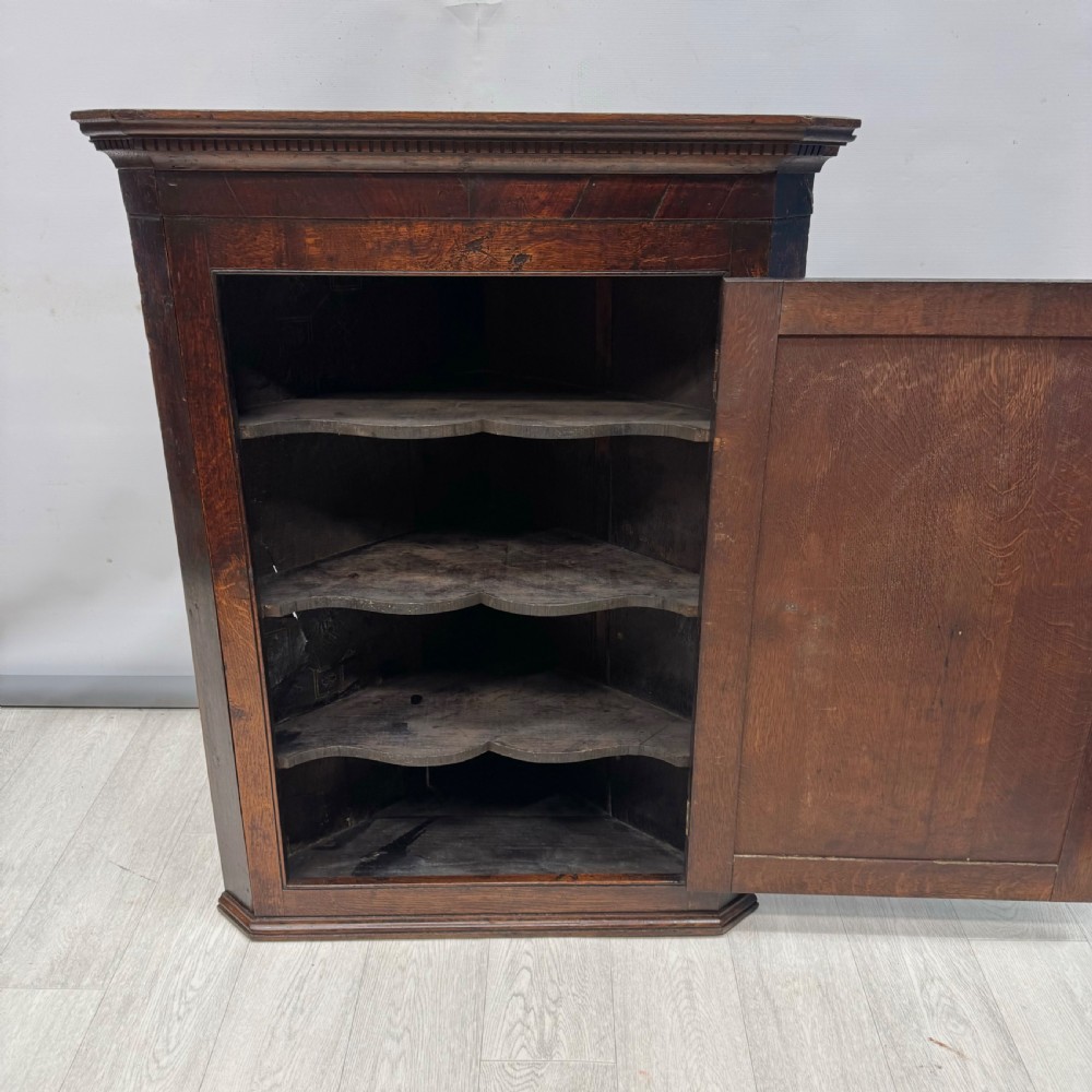An eighteenth-century Georgian dark oak corner cupboard featuring a single raised panel door with a decorative brass keyhole escutcheon and moulded cornice. View II