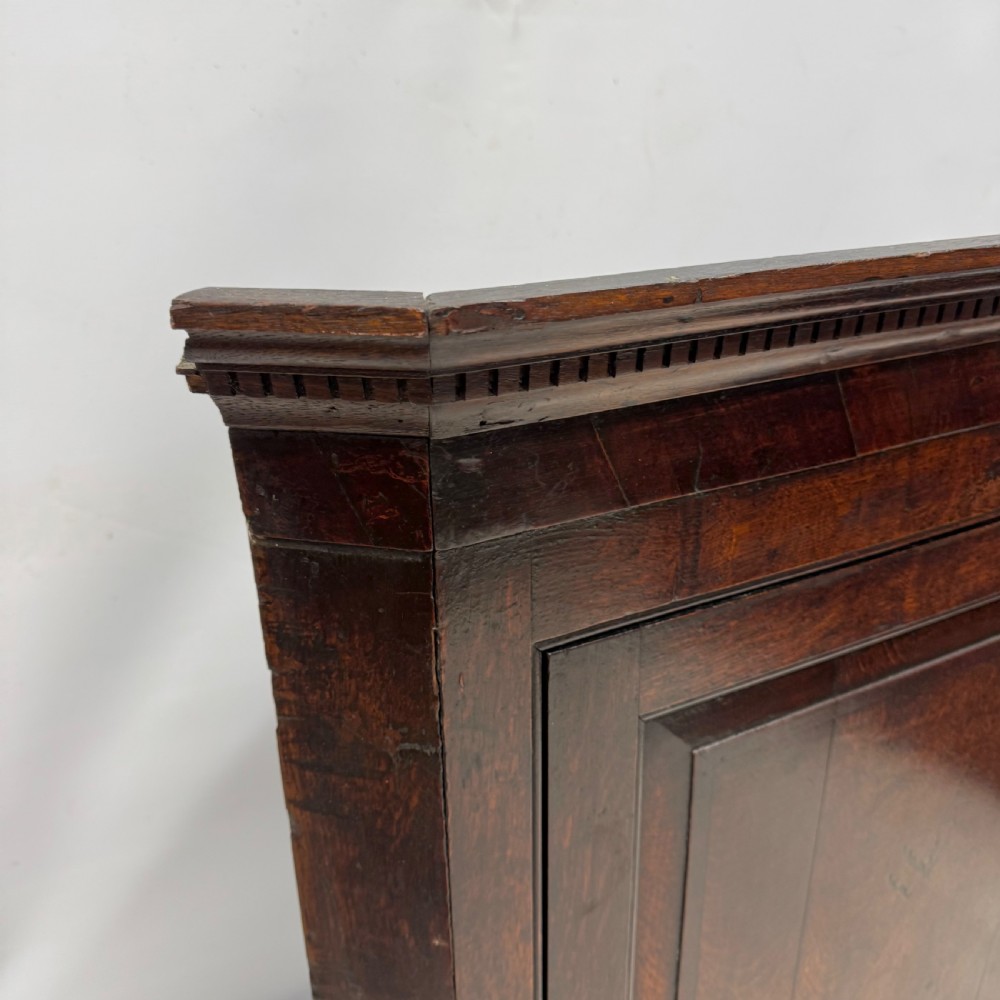An eighteenth-century Georgian dark oak corner cupboard featuring a single raised panel door with a decorative brass keyhole escutcheon and moulded cornice. View III
