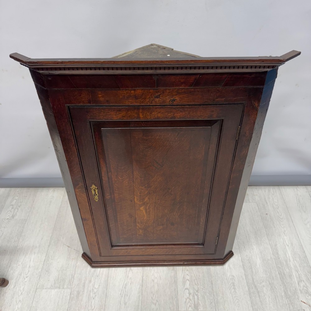 An eighteenth-century Georgian dark oak corner cupboard featuring a single raised panel door with a decorative brass keyhole escutcheon and moulded cornice. View IV