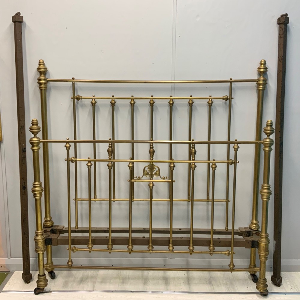 Victorian 5ft king-size brass bed frame featuring vertical spindles, turned finials, and a central cast decorative motif alongside original side rails.