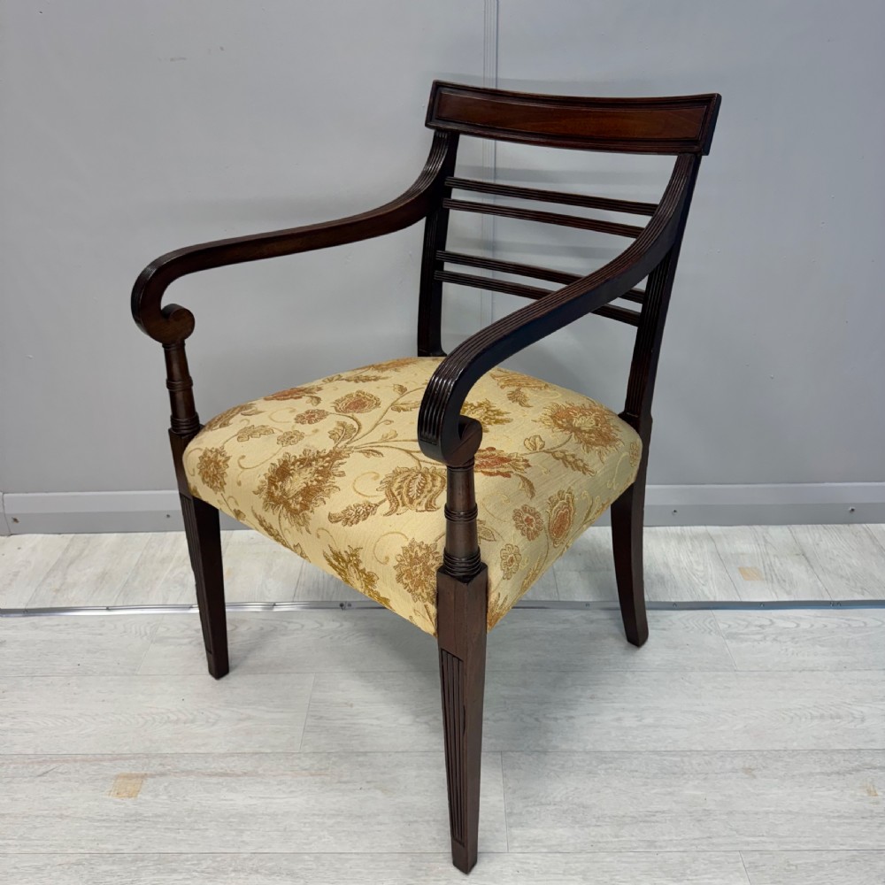 A dark mahogany Regency carver armchair featuring reeded scrolled arms, horizontal slat backrest, fluted front legs, and a golden floral patterned upholstered seat.