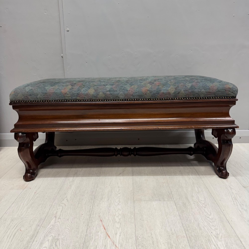 A Victorian mahogany piano duet stool featuring a patterned upholstered hinged top, brass studding, carved cabriole legs, and a turned stretcher base.