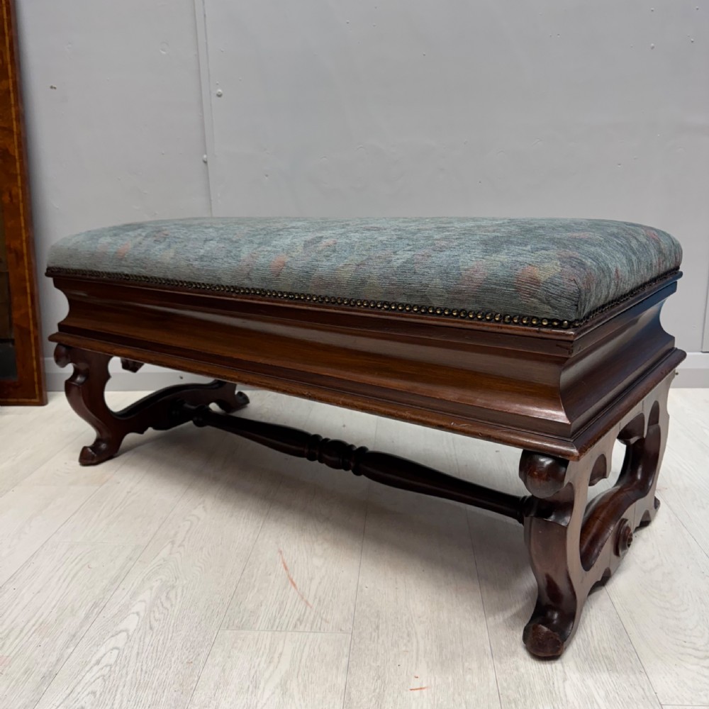 A Victorian mahogany piano duet stool featuring a patterned upholstered hinged top, brass studding, carved cabriole legs, and a turned stretcher base. View V