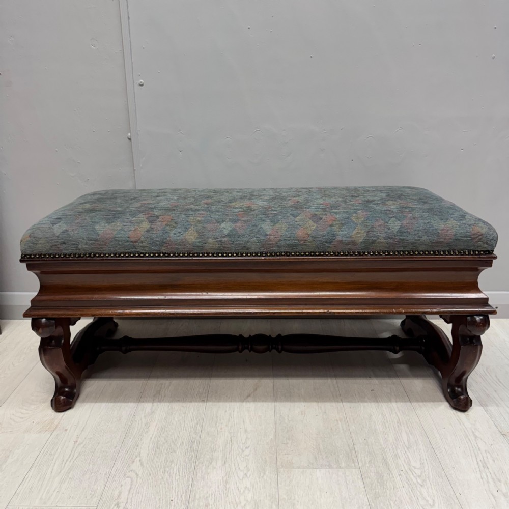 A Victorian mahogany piano duet stool featuring a patterned upholstered hinged top, brass studding, carved cabriole legs, and a turned stretcher base. View VI