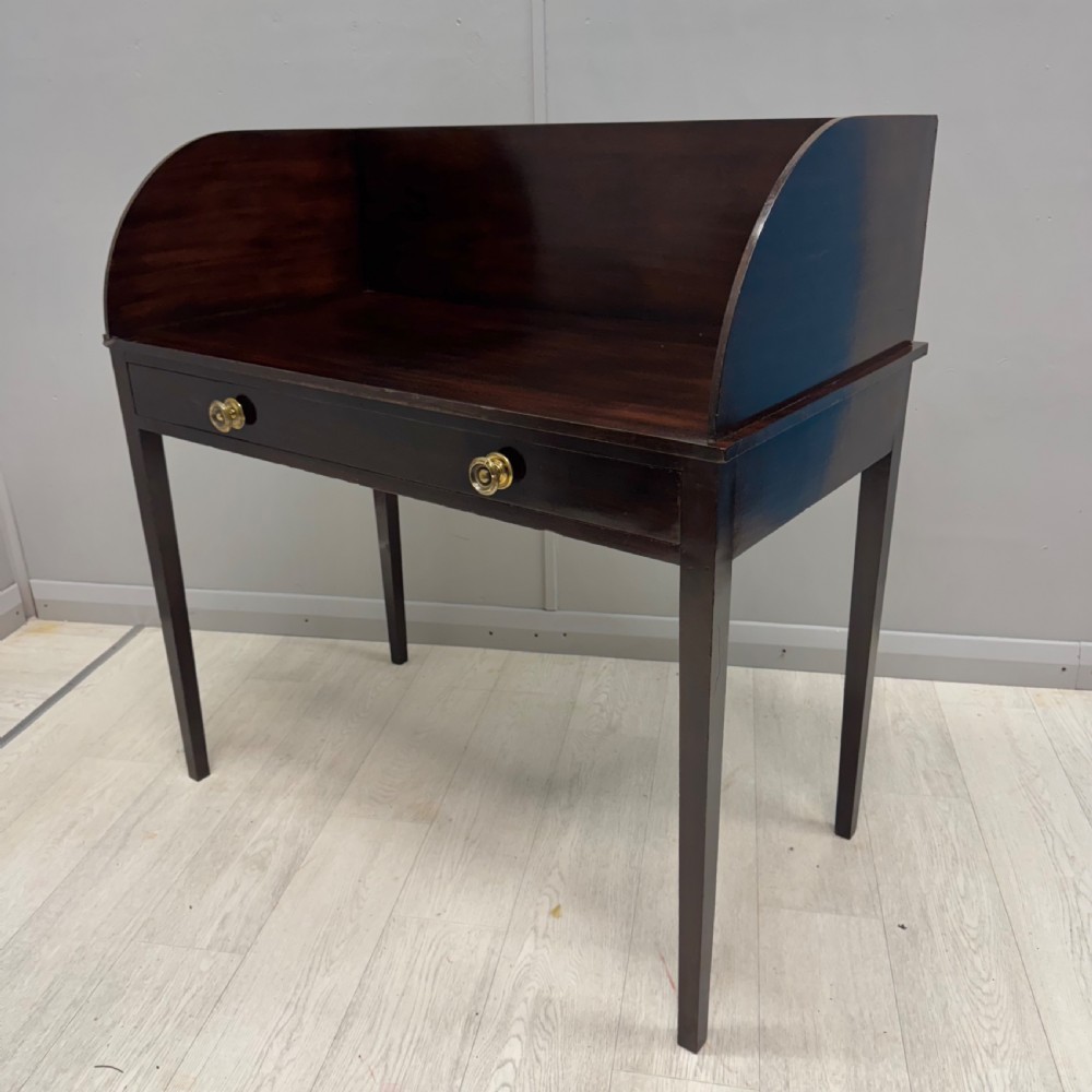 A dark mahogany Regency dressing table featuring a raised curved gallery back, a single drawer with two brass knobs, and four square tapered legs.