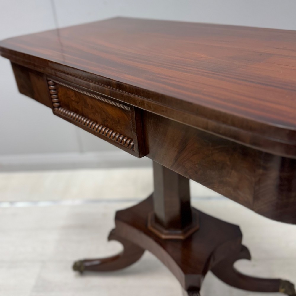 A Late Georgian dark mahogany fold-over side table featuring a beaded frieze, faceted pedestal base, and quadruped sabre legs with brass paw castors. View II