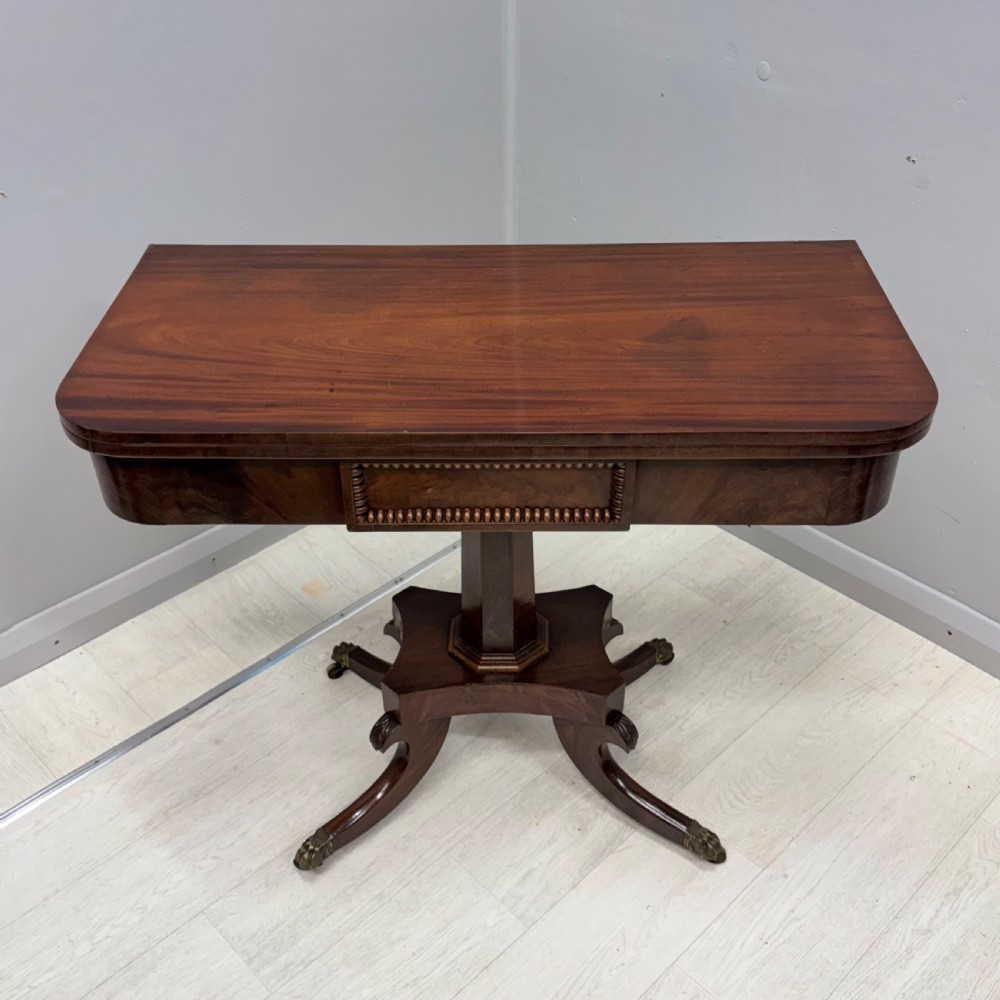 A Late Georgian dark mahogany fold-over side table featuring a beaded frieze, faceted pedestal base, and quadruped sabre legs with brass paw castors. View III