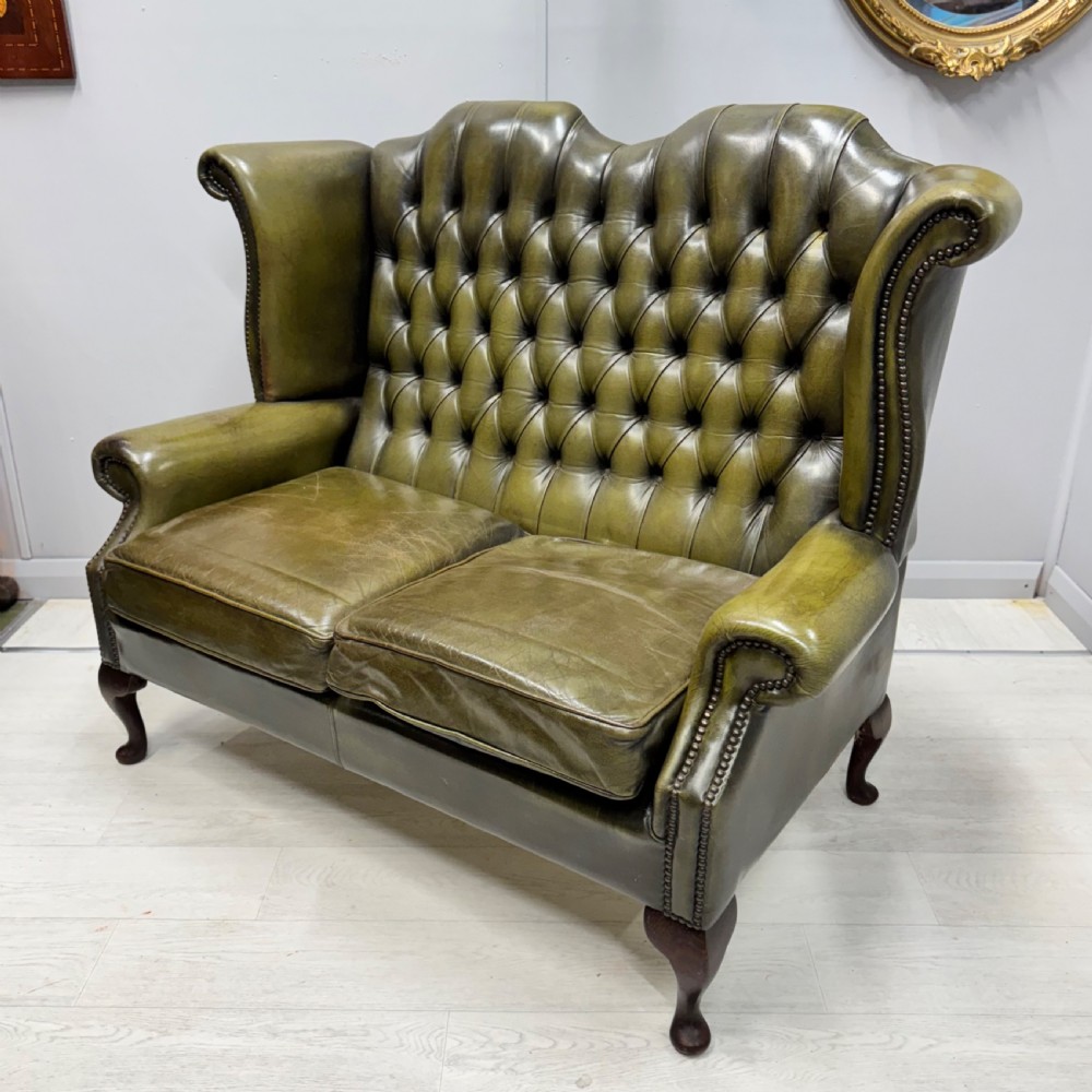 A two-seater high back sofa upholstered in deep-buttoned olive green leather with brass stud trimming and dark wooden cabriole legs.