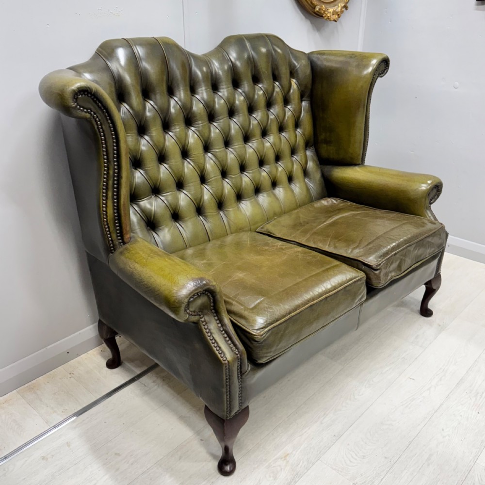 A two-seater high back sofa upholstered in deep-buttoned olive green leather with brass stud trimming and dark wooden cabriole legs. View V