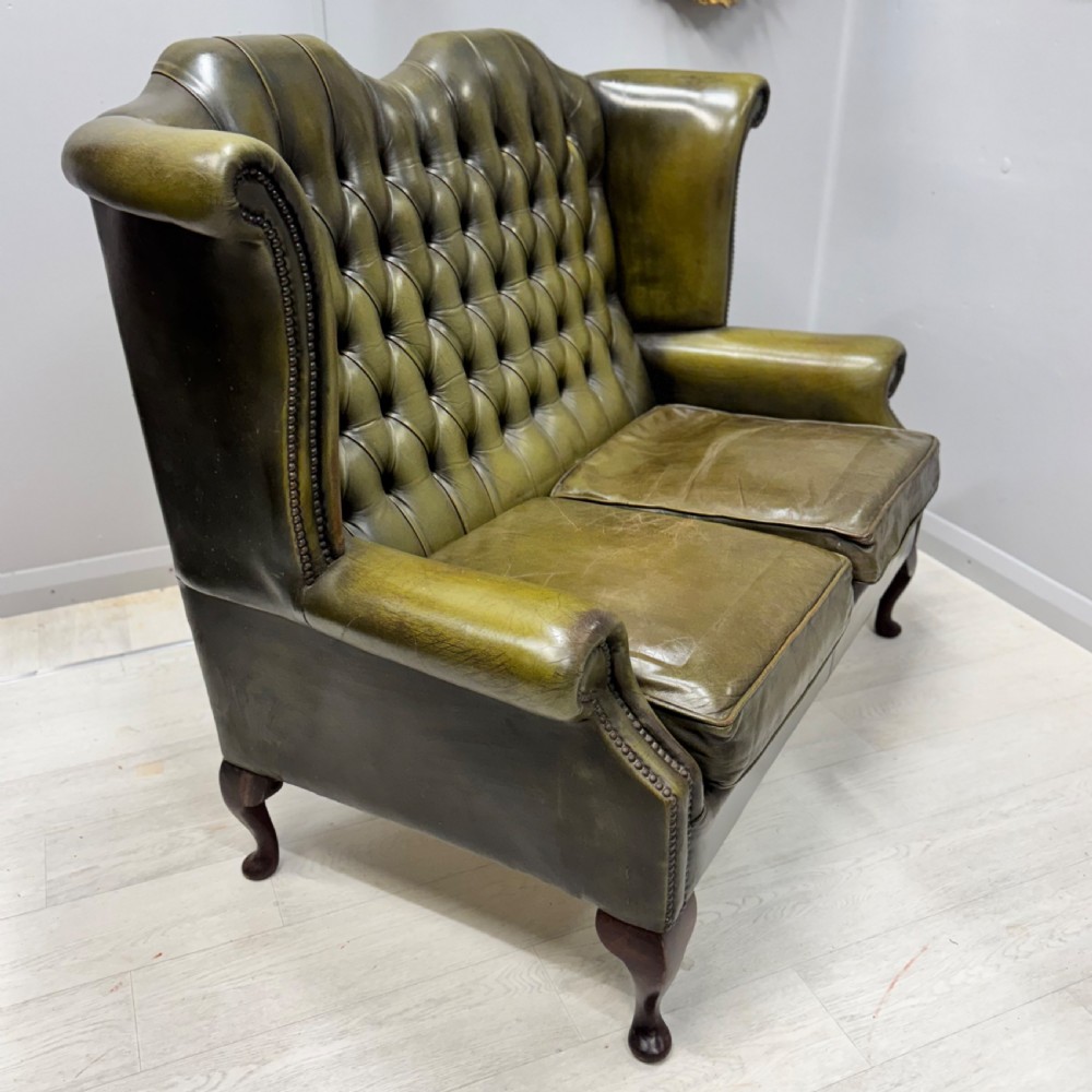 A two-seater high back sofa upholstered in deep-buttoned olive green leather with brass stud trimming and dark wooden cabriole legs. View VI
