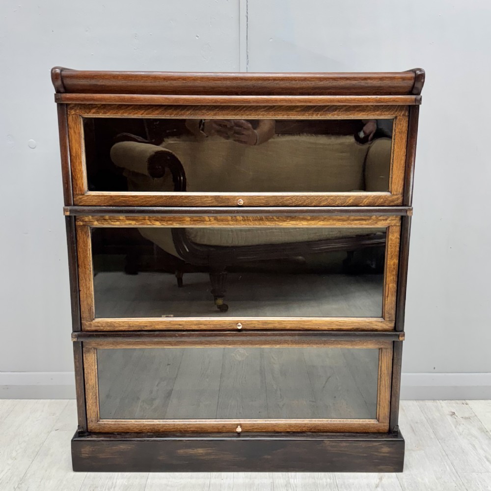 A three-tier oak Globe Wernicke stacking bookcase with glazed drop-down doors featuring small brass knobs.