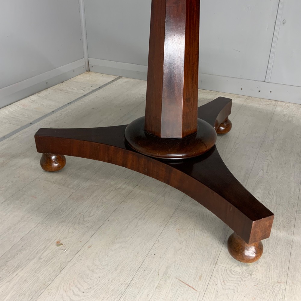 A circular Regency mahogany centre table featuring a smooth timber top supported on a central pedestal and a concave triform base with ball feet. View II
