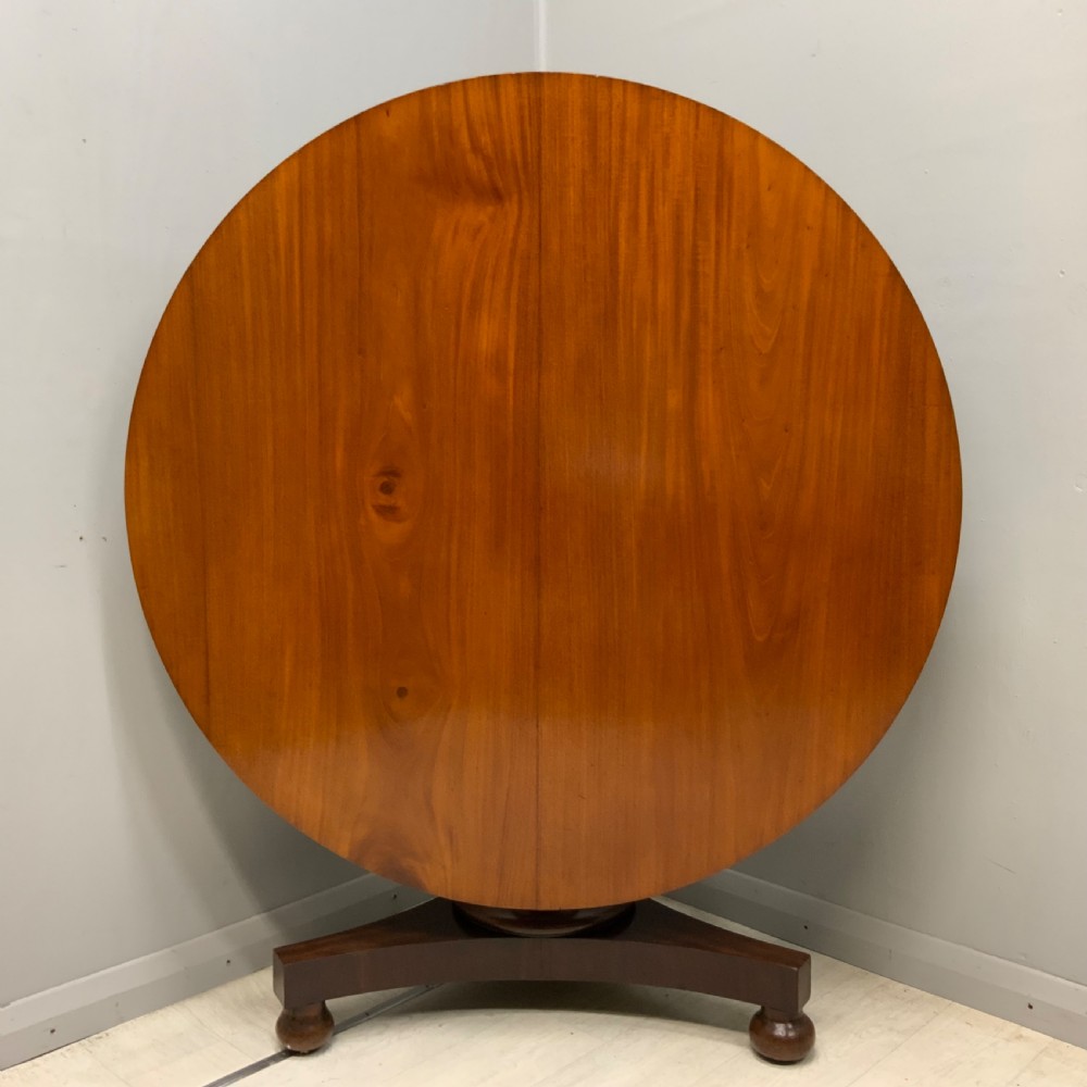 A circular Regency mahogany centre table featuring a smooth timber top supported on a central pedestal and a concave triform base with ball feet. View III