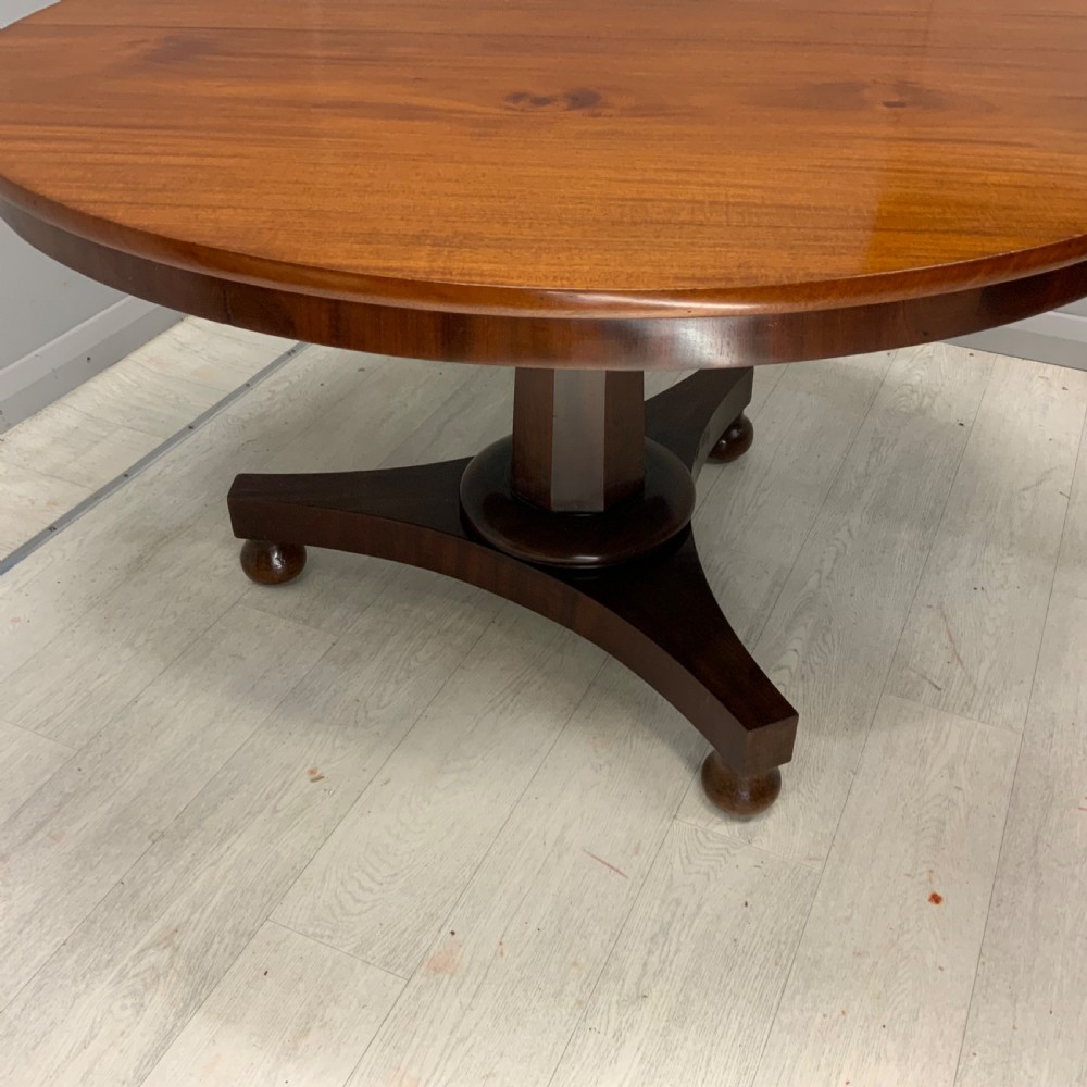 A circular Regency mahogany centre table featuring a smooth timber top supported on a central pedestal and a concave triform base with ball feet. View V
