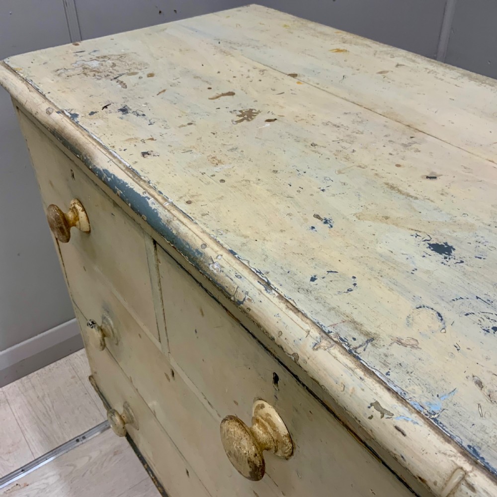A 19th-century painted pine chest of drawers featuring two short over two long drawers, turned wooden knobs, turned bun feet, and a distressed cream painted finish. View IV