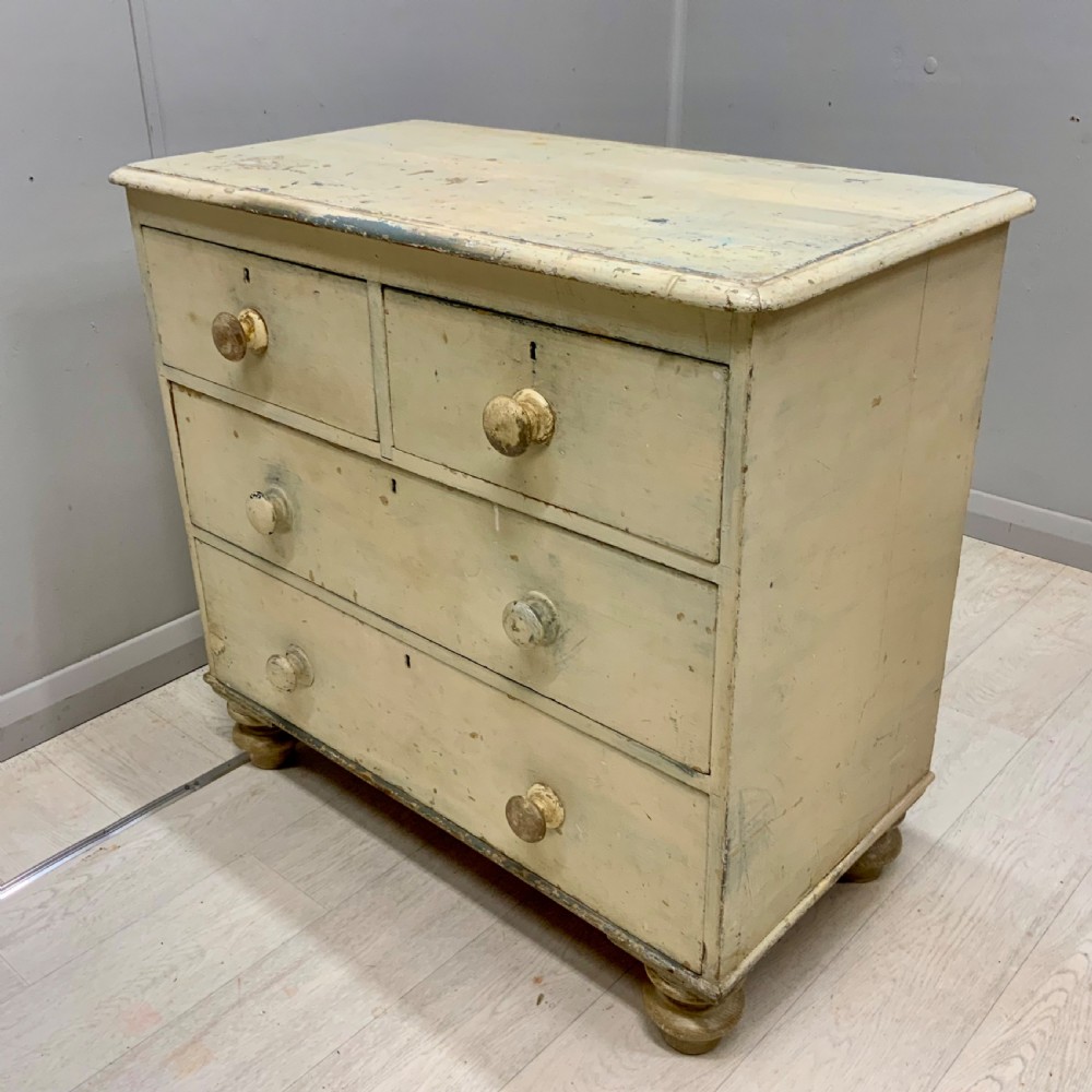 A 19th-century painted pine chest of drawers featuring two short over two long drawers, turned wooden knobs, turned bun feet, and a distressed cream painted finish. View V