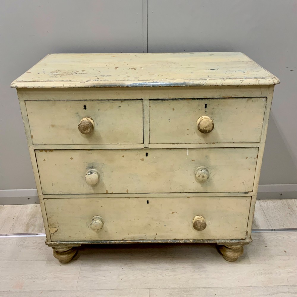 A 19th-century painted pine chest of drawers featuring two short over two long drawers, turned wooden knobs, turned bun feet, and a distressed cream painted finish. View VI