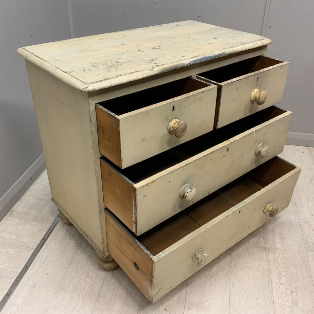 A 19th-century painted pine chest of drawers featuring two short over two long drawers, turned wooden knobs, turned bun feet, and a distressed cream painted finish. View VII