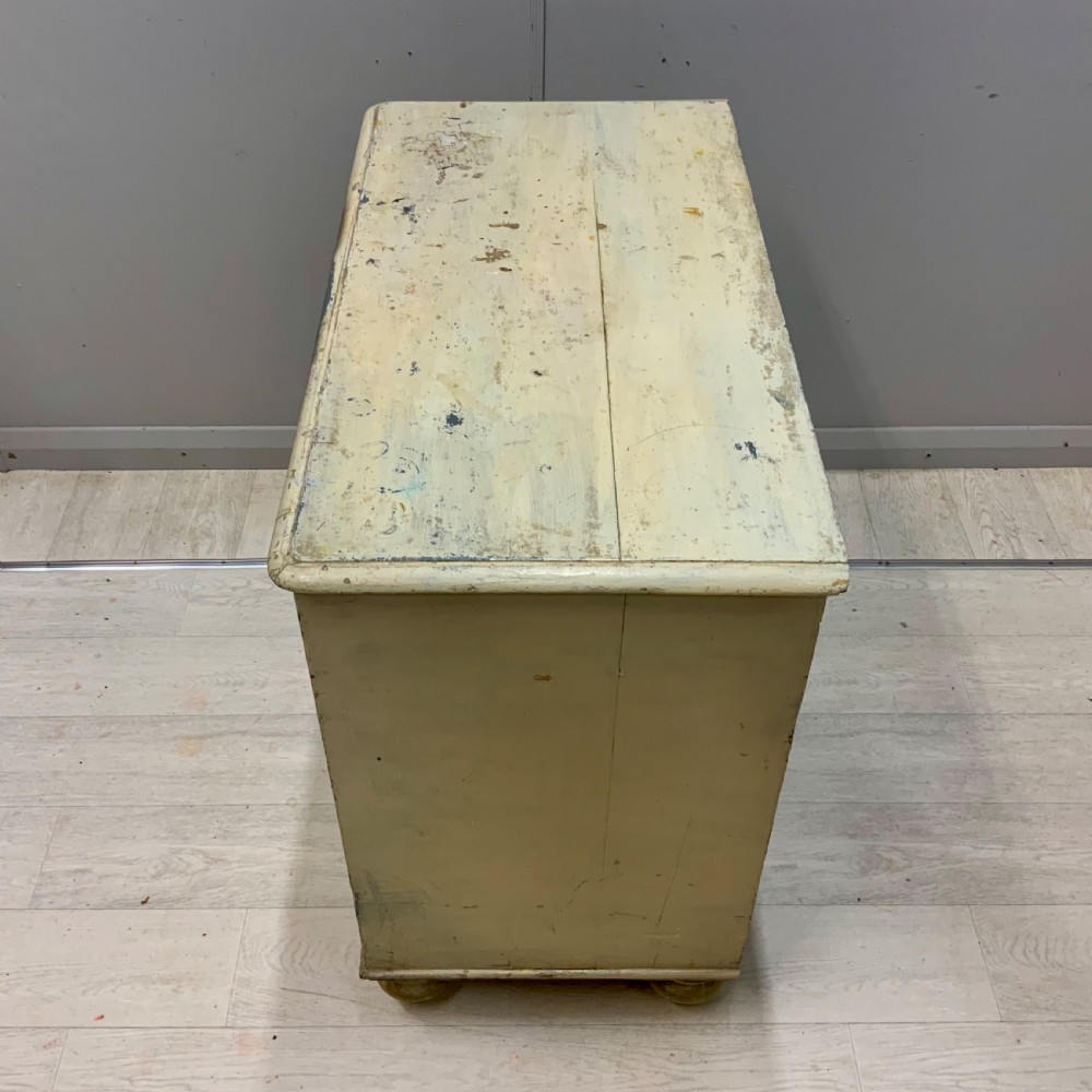 A 19th-century painted pine chest of drawers featuring two short over two long drawers, turned wooden knobs, turned bun feet, and a distressed cream painted finish. View IX