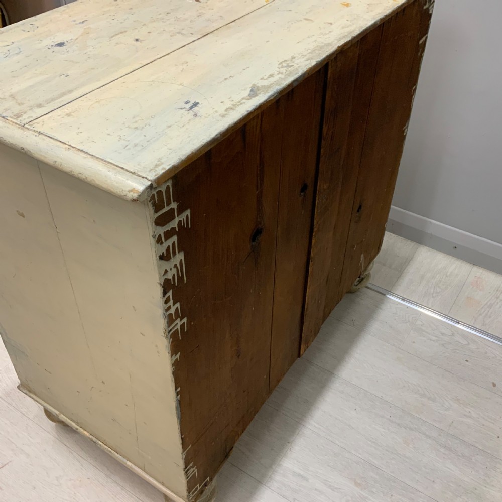 A 19th-century painted pine chest of drawers featuring two short over two long drawers, turned wooden knobs, turned bun feet, and a distressed cream painted finish. View X