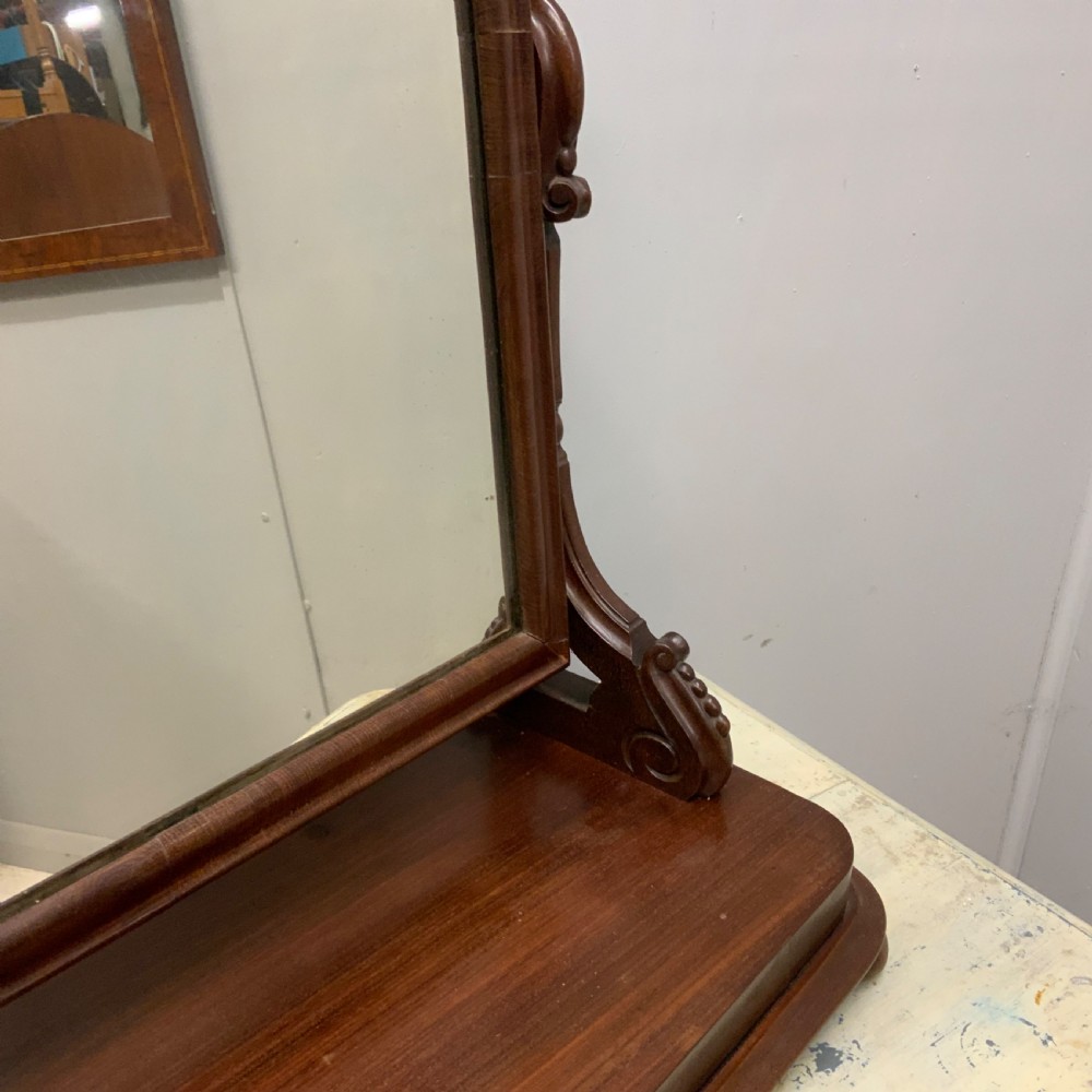 An antique Victorian mahogany toilet mirror featuring an arched glass frame supported by carved scroll uprights on a solid wooden plinth base. View II