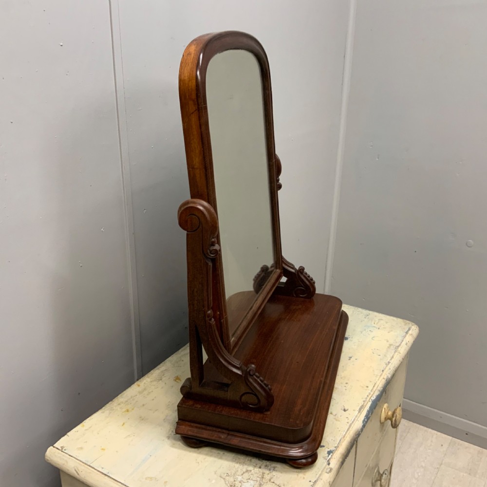 An antique Victorian mahogany toilet mirror featuring an arched glass frame supported by carved scroll uprights on a solid wooden plinth base. View III