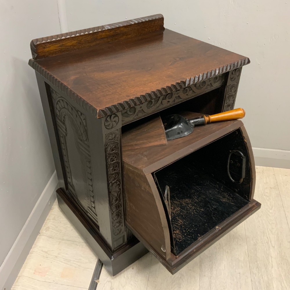 An Edwardian carved dark oak Purdonium coal box featuring a drop-front compartment, internal metal liner, and an included metal shovel with a wooden handle.