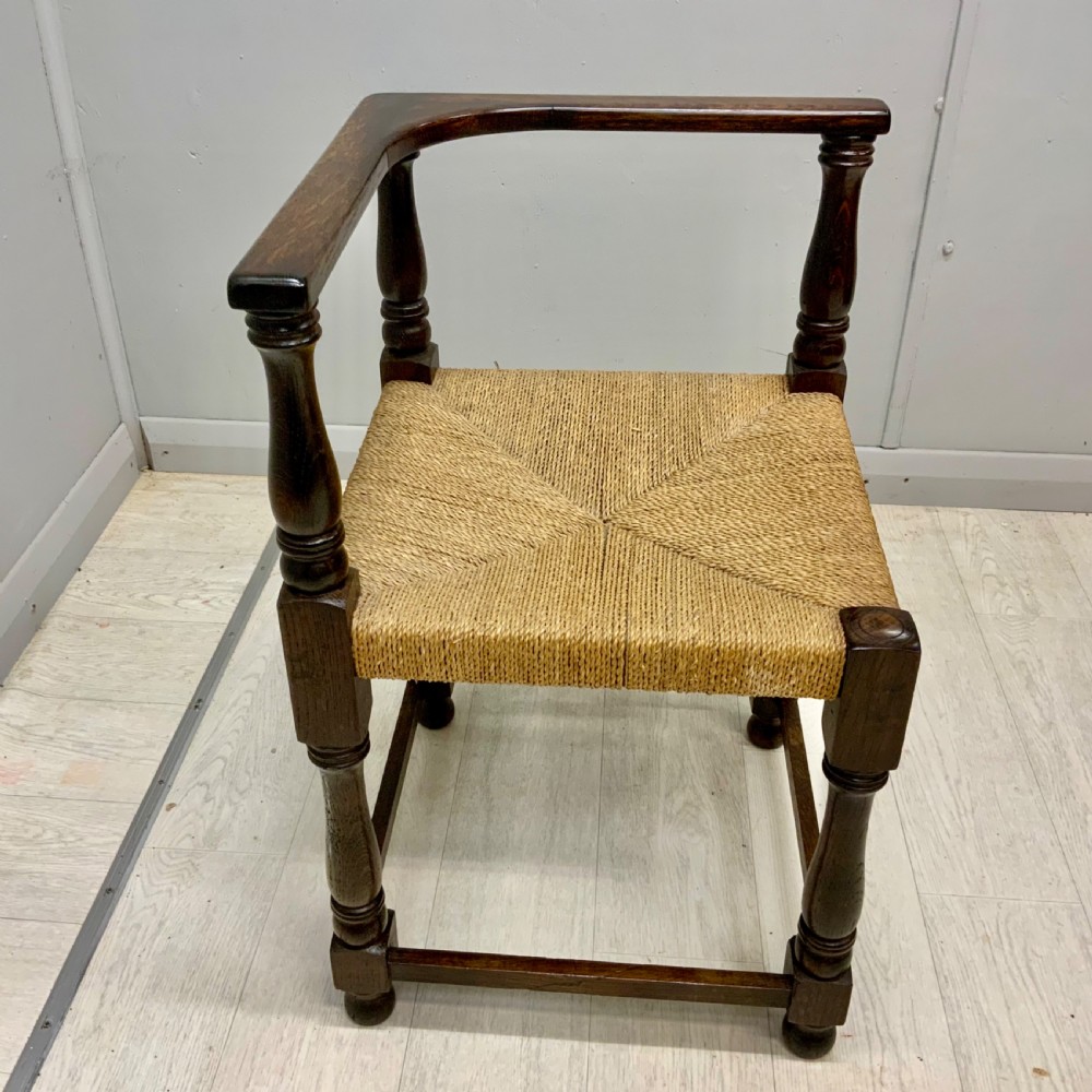 A dark oak corner chair featuring turned legs, a continuous curved armrest, and a hand-woven natural rush seat. View II