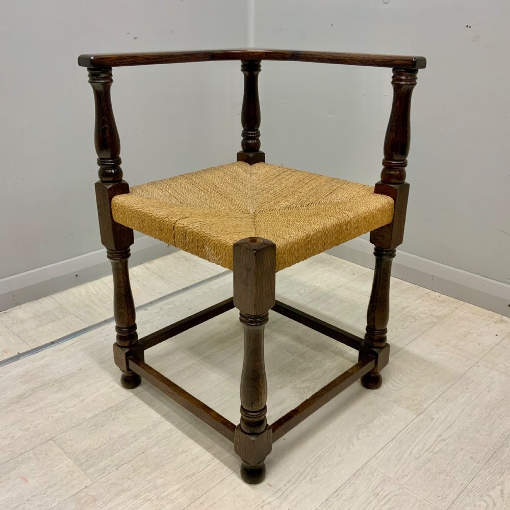 A dark oak corner chair featuring turned legs, a continuous curved armrest, and a hand-woven natural rush seat. View III