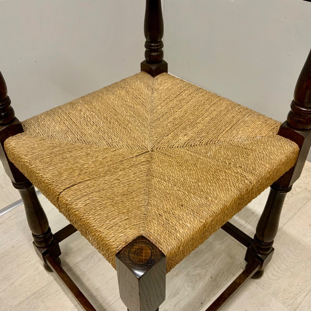 A dark oak corner chair featuring turned legs, a continuous curved armrest, and a hand-woven natural rush seat. View IV