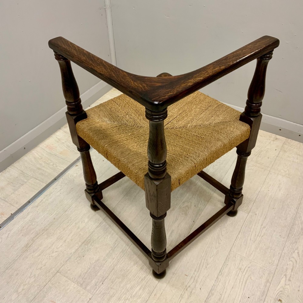 A dark oak corner chair featuring turned legs, a continuous curved armrest, and a hand-woven natural rush seat. View V