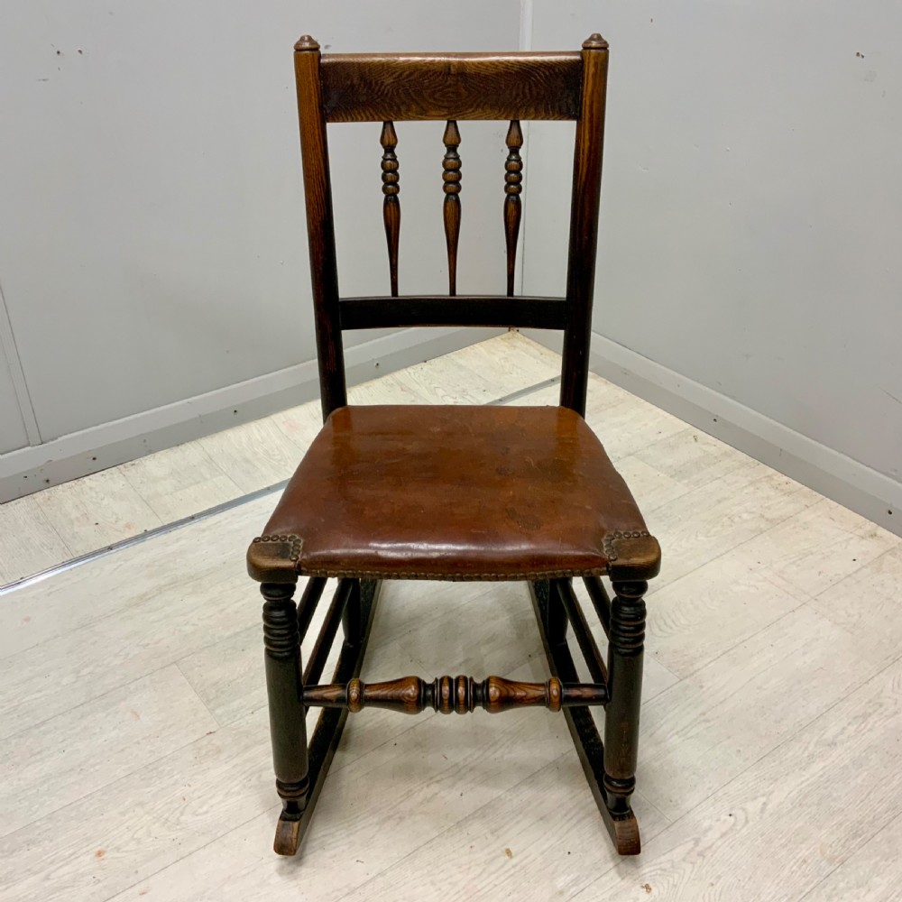 A mid-19th century dark oak rocking chair featuring a spindle backrest, a brown studded leather seat, and turned wooden front legs. View II