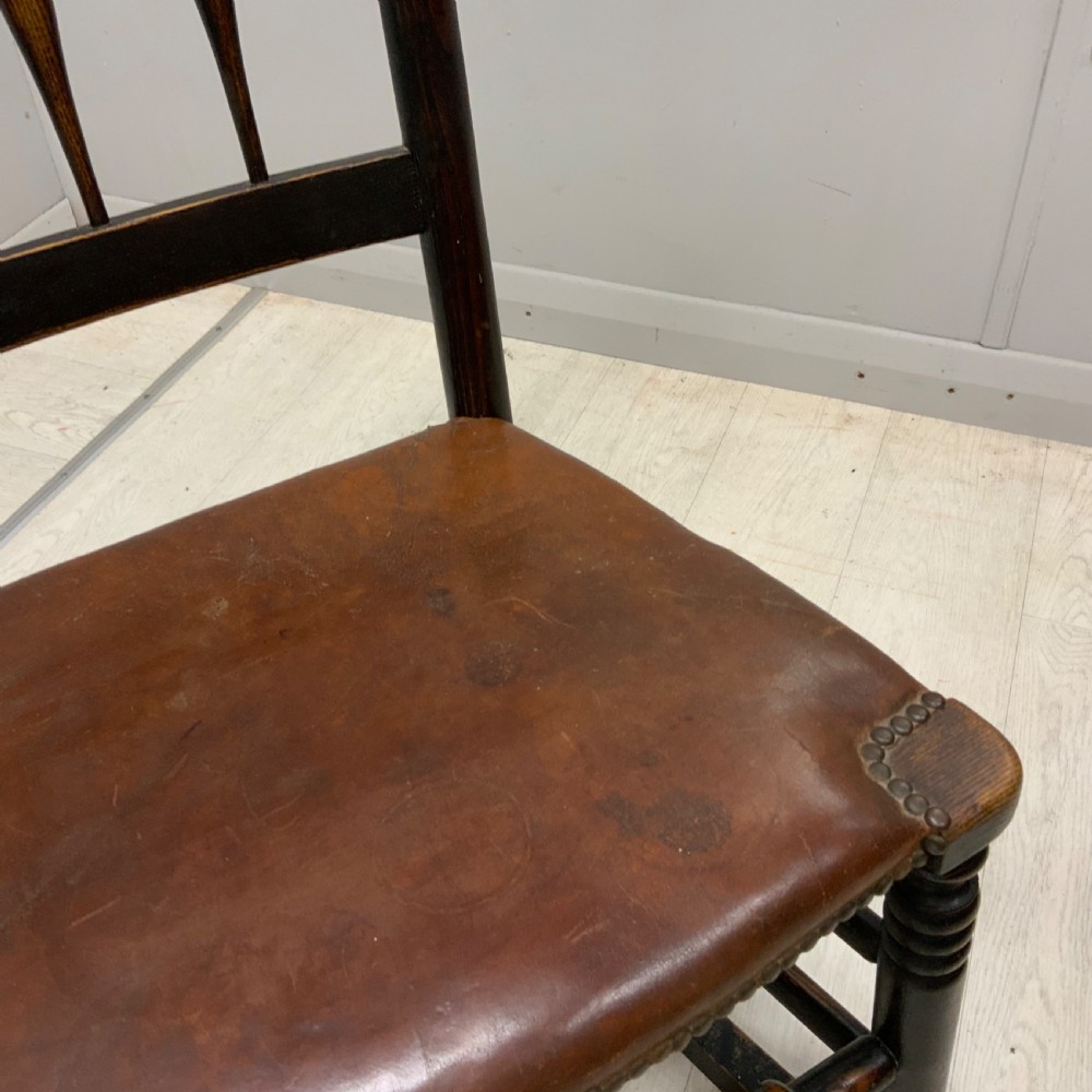 A mid-19th century dark oak rocking chair featuring a spindle backrest, a brown studded leather seat, and turned wooden front legs. View III
