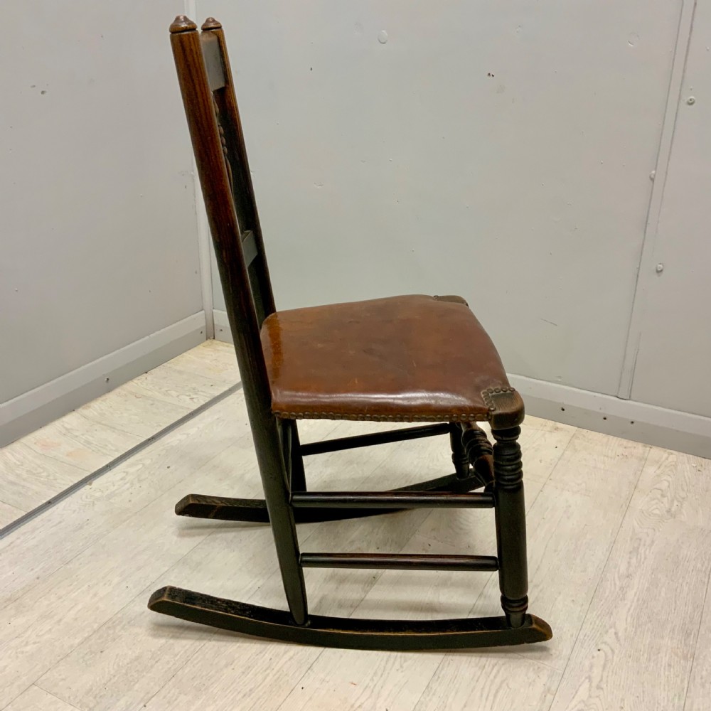 A mid-19th century dark oak rocking chair featuring a spindle backrest, a brown studded leather seat, and turned wooden front legs. View IV