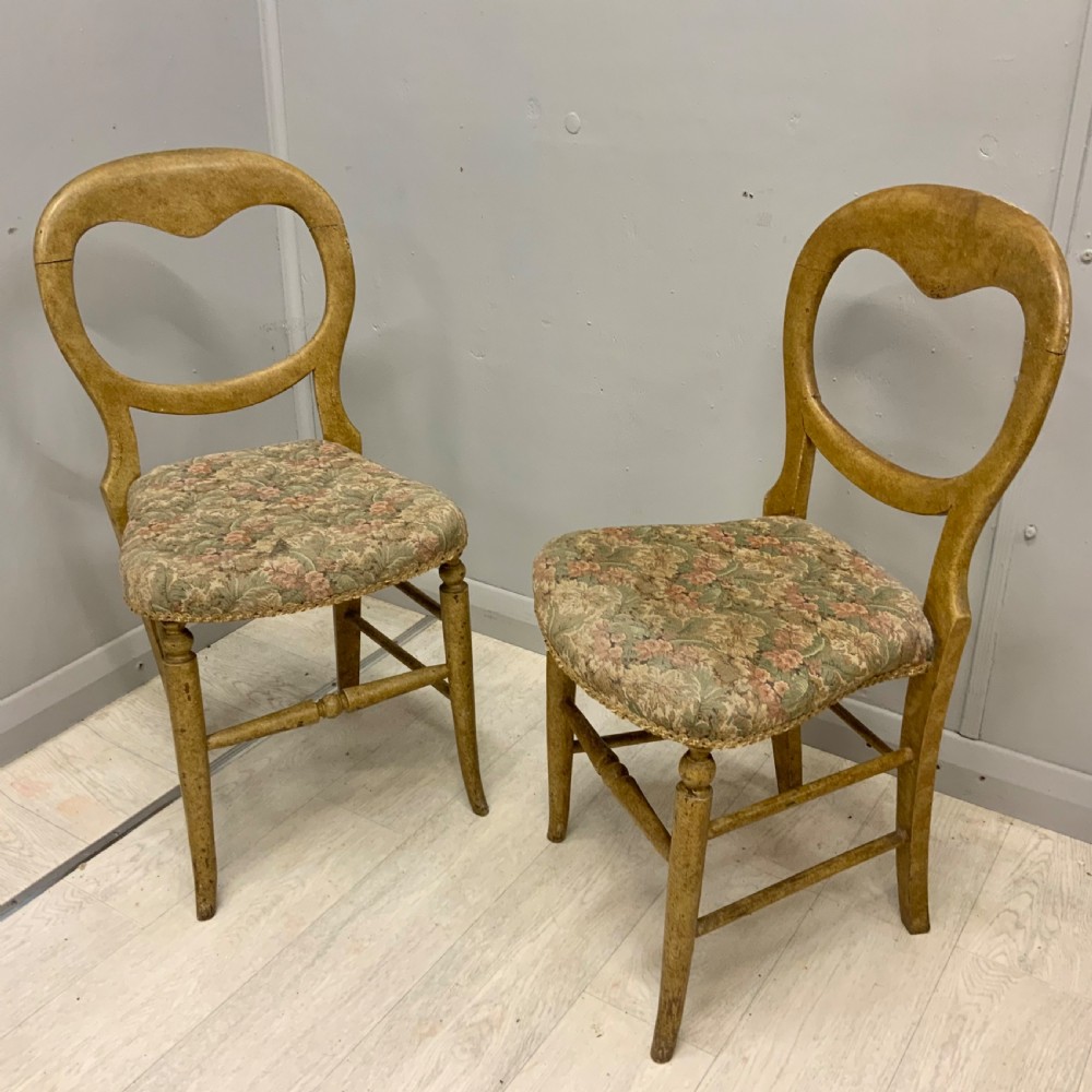 A pair of antique Victorian balloon back side chairs featuring ochre scumble glazed wood frames, turned legs, and floral tapestry upholstered seats.