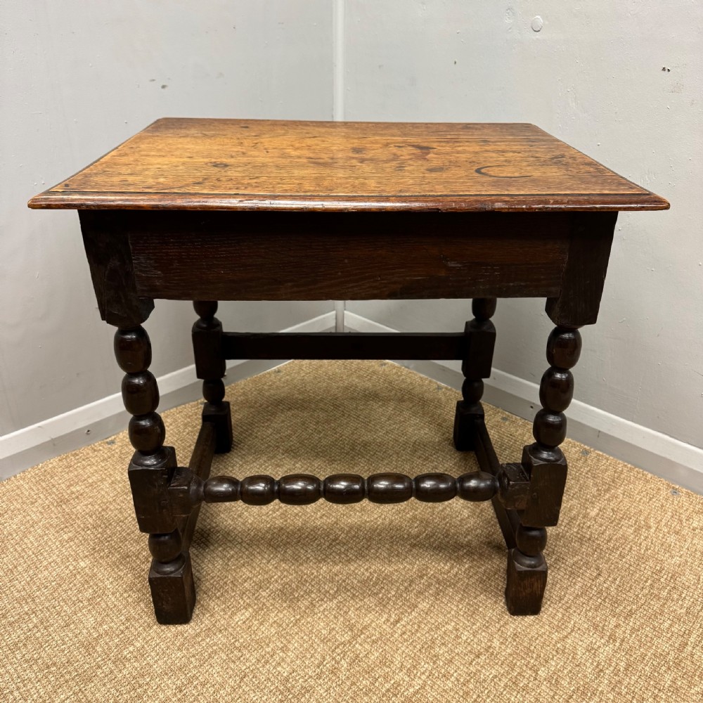 A 17th-century dark oak side table with a rectangular top, bobbin-turned legs, and connecting stretchers.