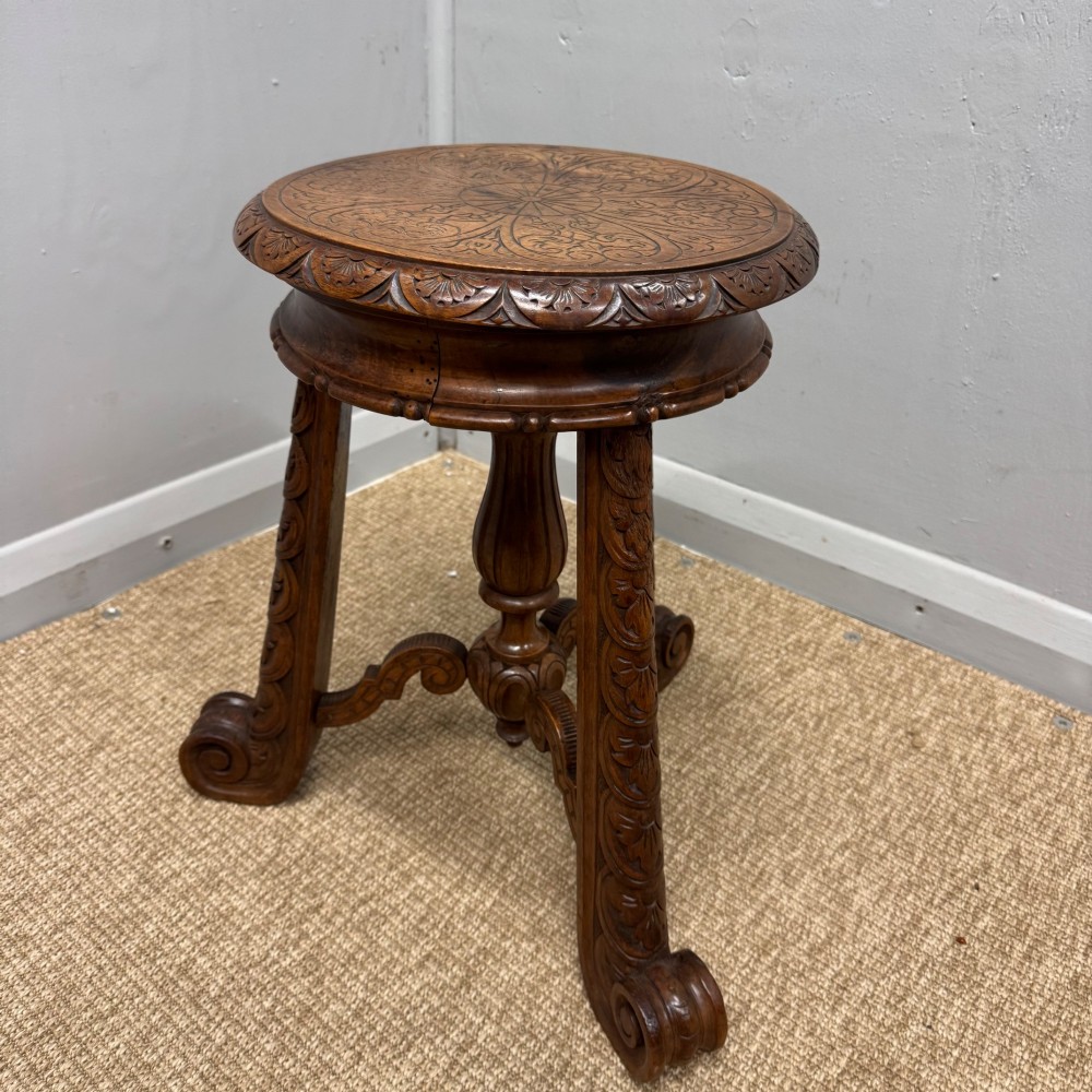 A carved dark hardwood revolving piano stool featuring a circular medallion seat, supported by three carved scroll legs and a central turned column.