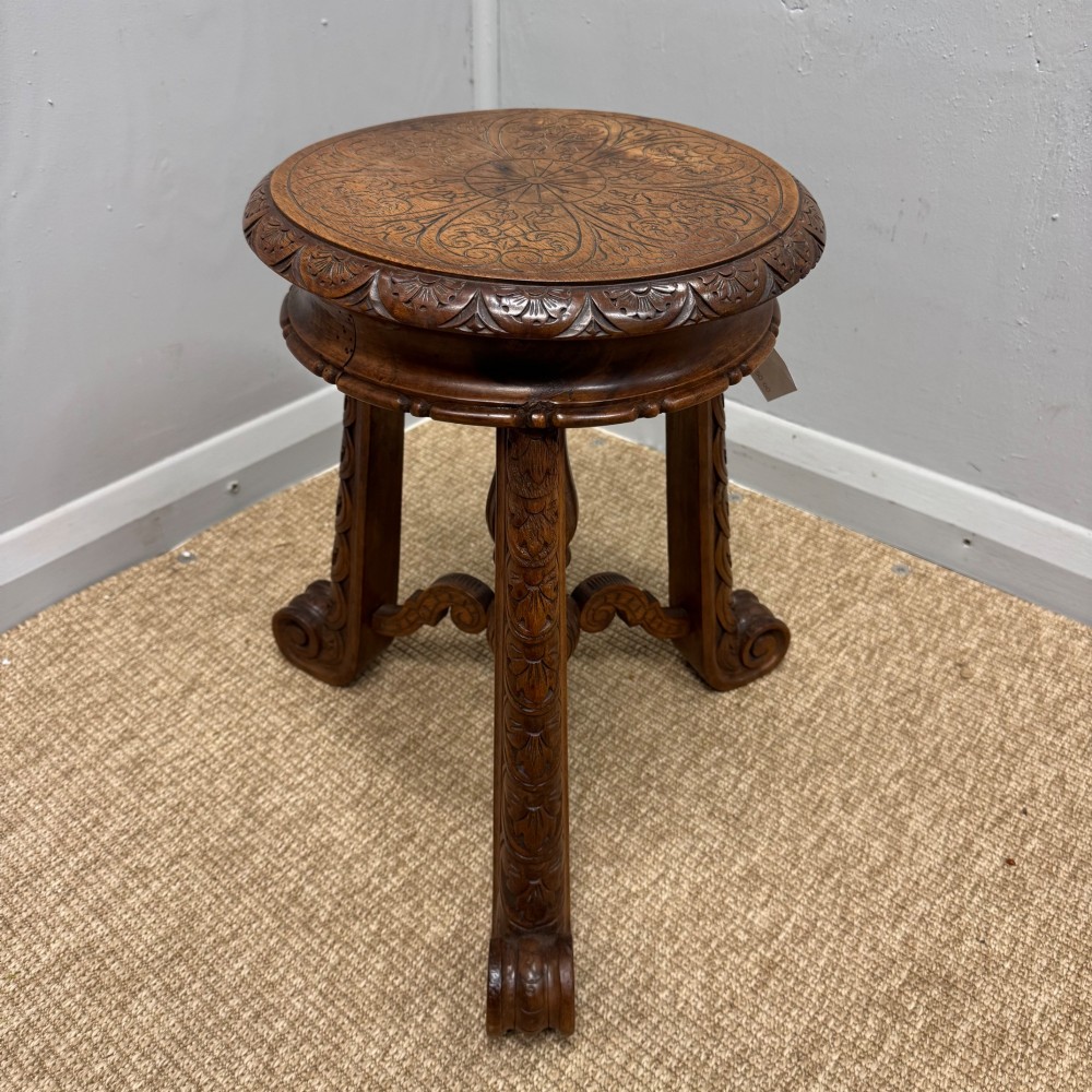 A carved dark hardwood revolving piano stool featuring a circular medallion seat, supported by three carved scroll legs and a central turned column. View III