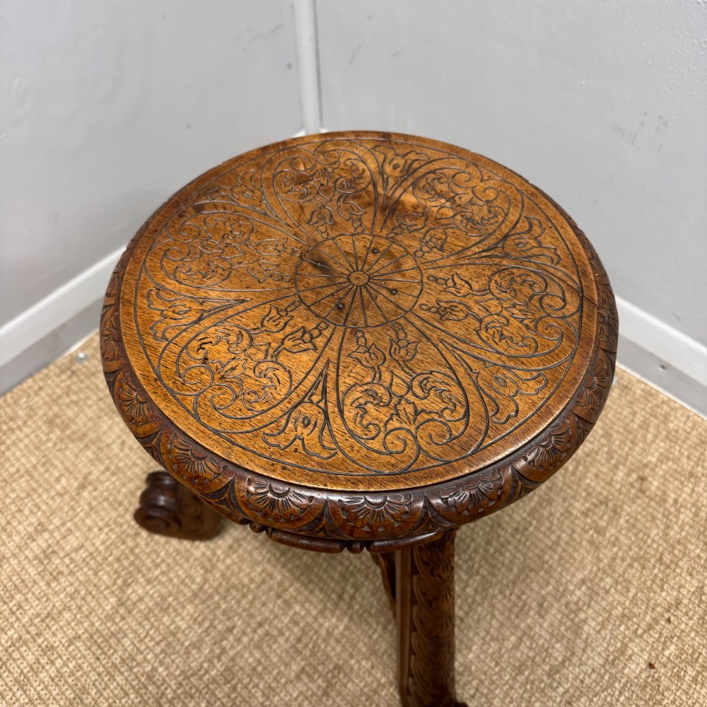 A carved dark hardwood revolving piano stool featuring a circular medallion seat, supported by three carved scroll legs and a central turned column. View V