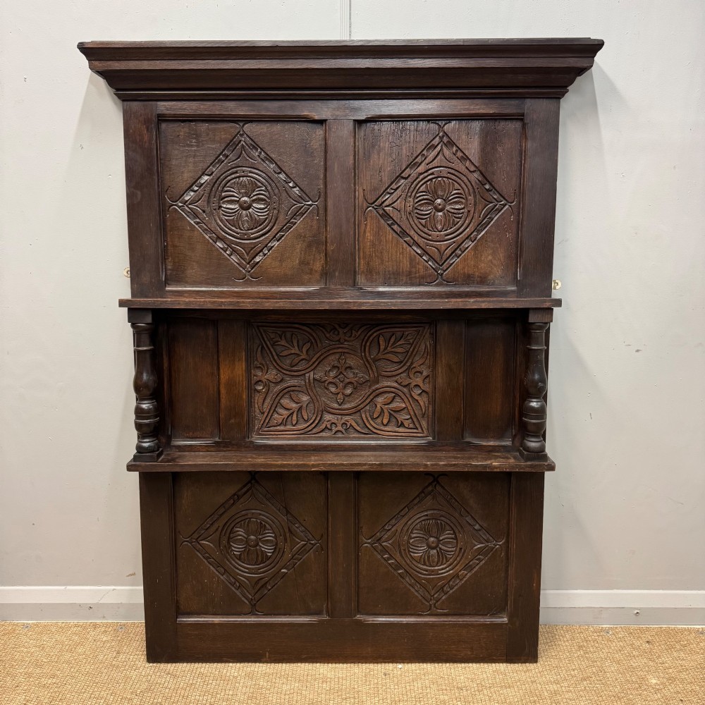 A 19th-century dark carved oak overmantel panel featuring carved geometric lozenges, a central foliate panel, turned spindle supports, and two display shelves.