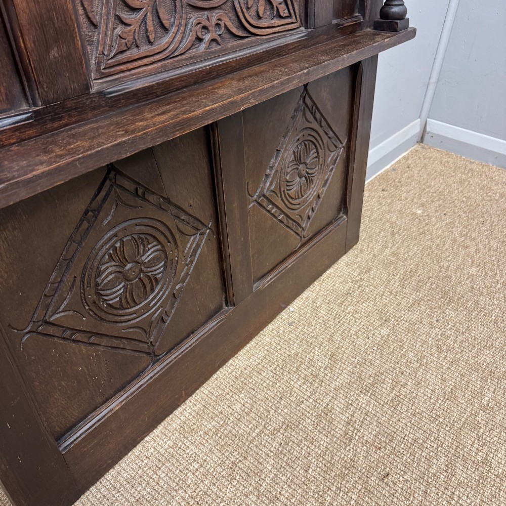 A 19th-century dark carved oak overmantel panel featuring carved geometric lozenges, a central foliate panel, turned spindle supports, and two display shelves. View III