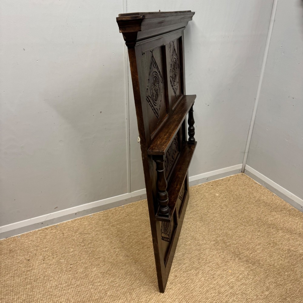 A 19th-century dark carved oak overmantel panel featuring carved geometric lozenges, a central foliate panel, turned spindle supports, and two display shelves. View V