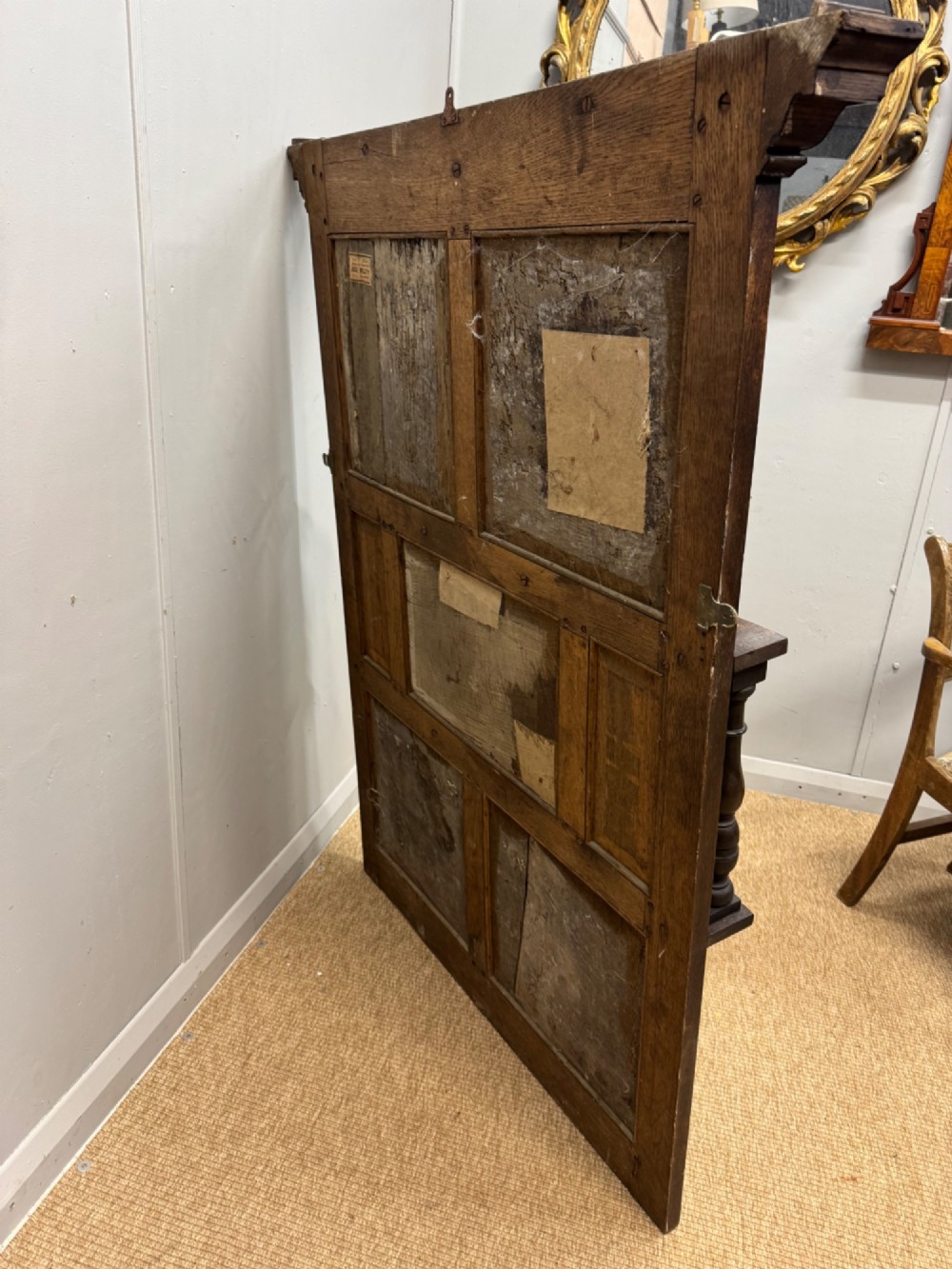 A 19th-century dark carved oak overmantel panel featuring carved geometric lozenges, a central foliate panel, turned spindle supports, and two display shelves. View VI